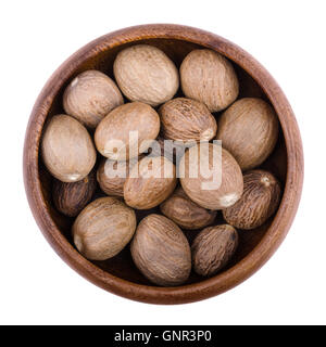 Nutmegs in a wooden bowl on white background. Myristica fragrans, also called pala, an edible brown and egg-shaped seed. Stock Photo