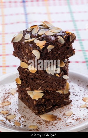stack of sweet dark brownies with almond slices on white plate Stock Photo