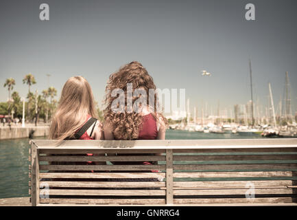 Two girls sitting on the bench watching the port of Barcelona - Spain Stock Photo