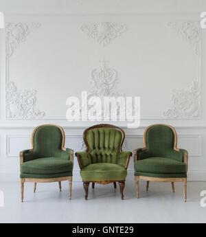 Set of green wooden vintage chairs standing in front a white wall design bas-relief stucco mouldings roccoco elements on light parquet floor. Stock Photo