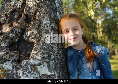 Closeup portrait of red-haired little girl in the woods. Stock Photo