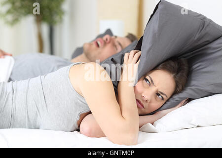 Man snoring while his wife is covering ears with the pillow Stock Photo