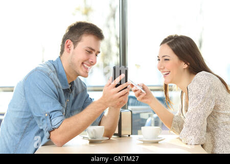 Happy couple sharing media content on line everyone with his smart phone in a coffee shop Stock Photo