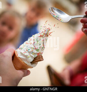 An ice cream cone with sprinkles being poured on top Stock Photo