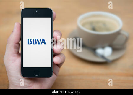 A man looks at his iPhone which displays the BBVA bank logo, while sat with a cup of coffee (Editorial use only). Stock Photo