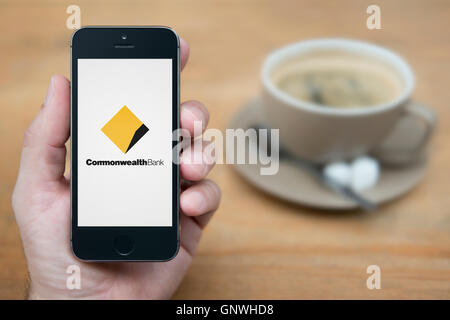 A man looks at his iPhone which displays the Commonwealth Bank logo, while sat with a cup of coffee (Editorial use only). Stock Photo