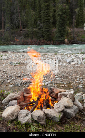 Campfire burning in rock ring beside the Wheaton river in Yukon Territory Canada in summer. Stock Photo