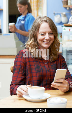 Woman In Coffee Shop Reading Text Message On Mobile Phone Stock Photo