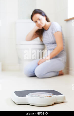 Unhappy Teenage Girl Sitting On Floor Looking At Bathroom Scales Stock Photo