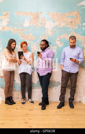 Group of young people standing in front of a grunge wall with a mobile phone hands Stock Photo