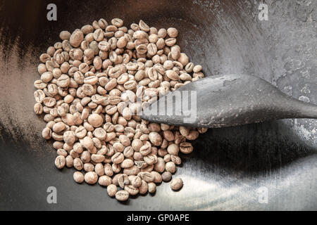 Green coffee beans in the pan with an old wooden bowl, ready to be roasted. Stock Photo