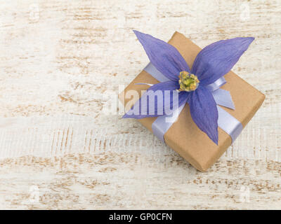 Gift box wrapped in brown kraft paper with satin ribbon and violet four petals  flower on the white wooden painted board Stock Photo