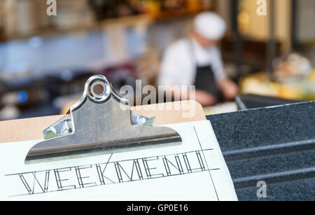 Week menu clipboard with restaurant and cook in the background. Stock Photo