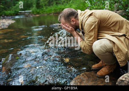 Tourist refreshing his face from river Stock Photo