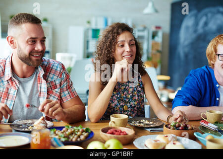 Friendly young people sitting by table and having dinner Stock Photo
