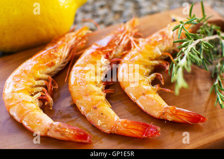 Grilled Shrimps Served on a Wooden Plate With Lemon and Rosemary. Three Grilled Seasoned Shrimps Closeup. Stock Photo