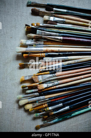 Top view of various and multicolored brushes covered in paint laying on cloth. Stock Photo