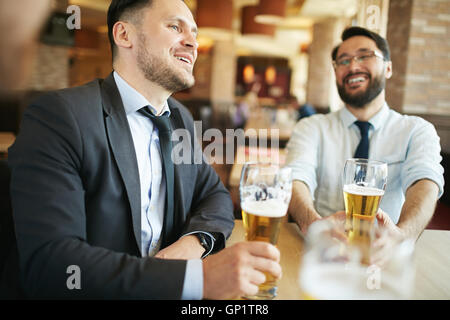 Two formally dressed laughing businessmen chatting and having beer in bar. Stock Photo