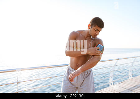 Serious african young sportsman using his smartphone outdoors at the sea pier Stock Photo