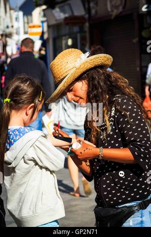 A lady street artist putting a senna tattoo on a young girl's arm in Newquay, Cornwall, UK Stock Photo