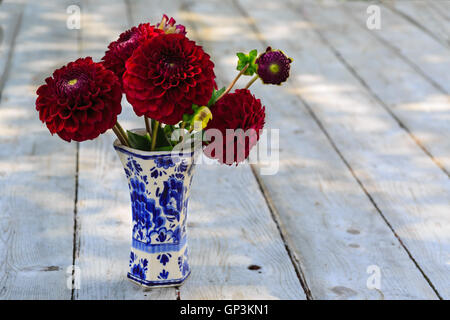 Home garden burgundy dahlias in a delft pottery vase under dappled shade. Stock Photo