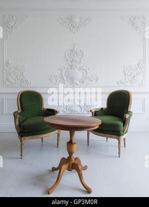 Luxury clean bright white interior with a old antique vintage green chairs over wall design bas-relief stucco mouldings roccoco elements Stock Photo