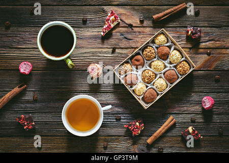 Sweet desserts: chocolate truffles, chocolate candy barks, cup of coffee, cup of green tea, cinnamon stick and coffee on table Stock Photo