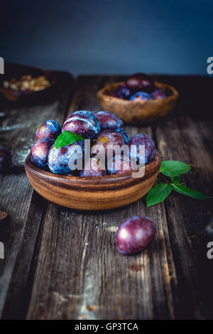 Fresh purple plums in bowl on wooden table. Vertical Stock Photo