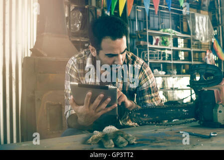 Man referencing chainsaw repair instructions on digital tablet Stock Photo