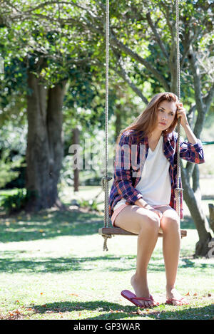 Young woman sitting on park swing with sad expression on face Stock Photo