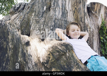 Boy leaning against big tree trunk Stock Photo