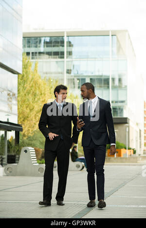 Businessmen having conversation while walking on sidewalk Stock Photo