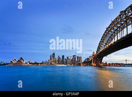 Waterfront of Sydney city CBD around Circular Quay with Harbour bridge as seen across blurred blue waters of Harbour at sunset. Stock Photo
