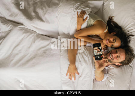 Couple taking selfie with smartphone while lying in bed Stock Photo