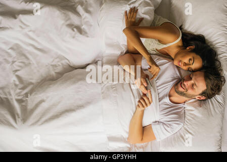 Couple using smartphone together while lying in bed Stock Photo