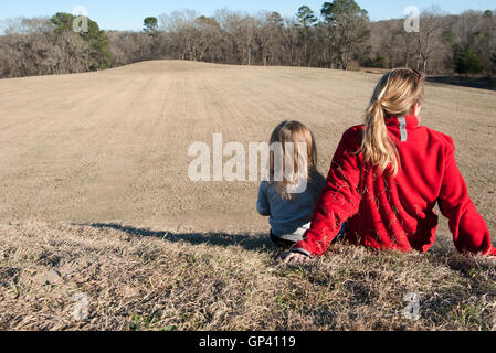 Mother and daughter sitting together on hill, rear view Stock Photo