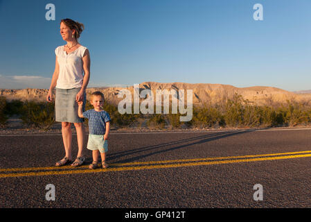 Mother and toddler son walking together on paved road through desert Stock Photo