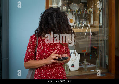 A woman in a red dress, with her face covered by her hair, is busy on her smart mobile phone - Plymouth, 1st September 2016