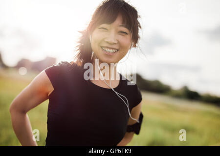 Portrait of happy female running standing outdoors and smiling at camera. Chinese female model in sportswear and earphone at cit Stock Photo