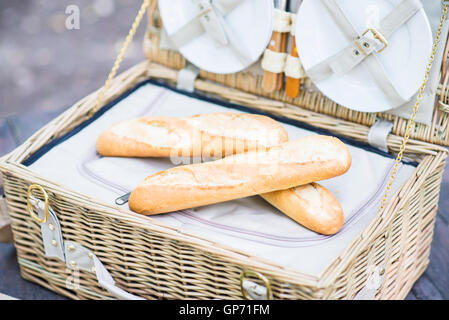 Open picnic basket with bread inside over a wooden table in the park. Stock Photo