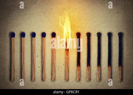 Burning match standing middle a row of whole, new matches at left and extinguished at right. Leadership concept Stock Photo