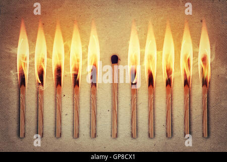 Whole, unused match standing middle a row of burning matches. Standing out from the crowd, leadership concept Stock Photo