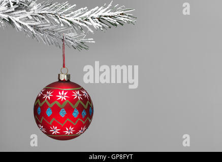 Snow covered Christmas tree with a red hand painted Bauble hanging on a grey background Stock Photo
