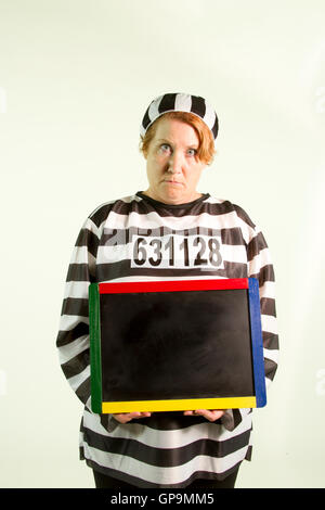 Mature woman in prison uniform holding chalkboard on white background. Stock Photo