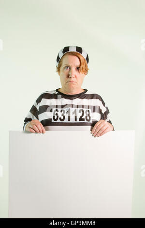 Mature woman in prison uniform holding plain white sign on white background. Stock Photo