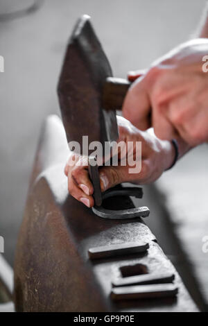 Blacksmith forges a horseshoe. Hammering glowing steel. Stock Photo
