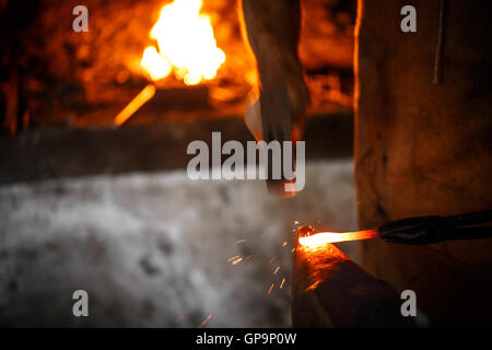 The blacksmith manually forging the molten metal on the anvil in smithy Stock Photo