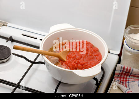 Cooking the Bolognese sauce, also called ragu, in the kitchen at home. Onion, tomato and meat in the pot with a wooden spoon. Stock Photo