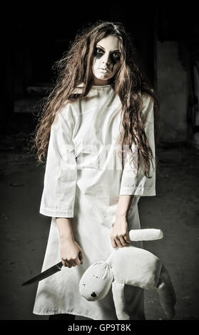 Horror style shot: a strange sad girl with moppet doll and knife in hands Stock Photo