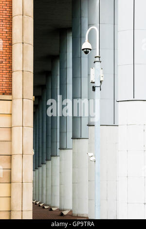 CCTV camera placed at the entrance to a pillared walkway by an urban office block Stock Photo